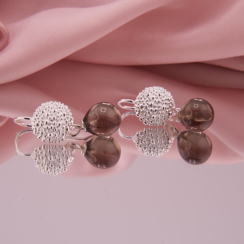 Ohrringe mit granulierten Halbkugeln aus Sterling Silber und frei schwingenden Rauchquarz Tropfen, liegend auf einer Spiegeloberfläche präsentiert.